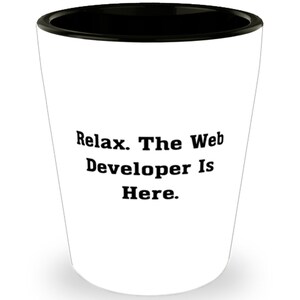 May include: White ceramic shot glass with a black rim. The glass has the text "Relax. The Web Developer Is Here." printed on it.
