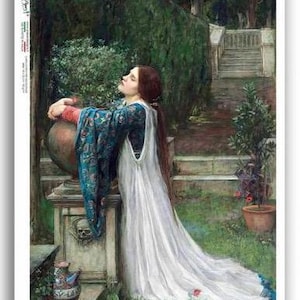 May include: A woman in a white gown and blue robe is kneeling by a stone urn in a garden setting. She has her head tilted back and her eyes closed, as if in prayer. The garden is lush and green, with trees and shrubs in the background.
