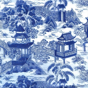 May include: A fabric or paper surface featuring a blue and white chinoiserie pattern. The design depicts a landscape with pagodas, arched bridges, stylized trees, and rocky terrain. The intricate illustration is rendered in a monochromatic blue ink.