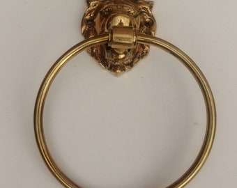 Könnte beinhalten: Goldfarbener Handtuchring aus Metall mit einem Löwenkopf-Design. Der Ring ist rund und hat eine glatte, polierte Oberfläche.