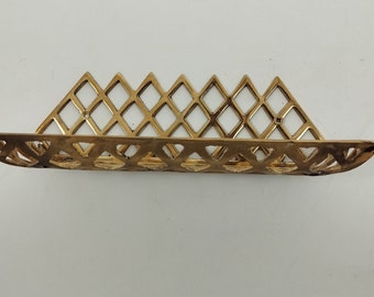 May include: Gold metal wall shelf with a diamond pattern. The shelf is curved and has a decorative design.