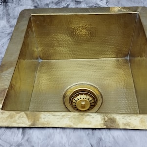 May include: A square, hammered brass kitchen sink with a drain in the centre.