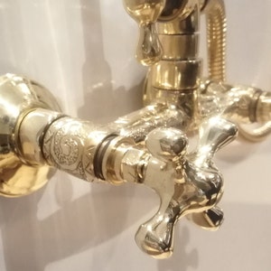 Unlacqured brass brass shower system with curved wall tube, wall faucet, cross knobs, round brass shower head and shower hose.