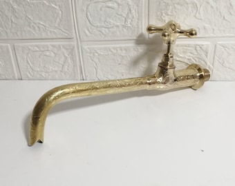 Puede incluir: Un grifo de color dorado con un diseño ornamentado y un caño largo y curvo. El grifo está montado en una pared blanca.