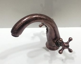 May include: A copper-coloured bathroom faucet with an ornate design and two cross-shaped handles.