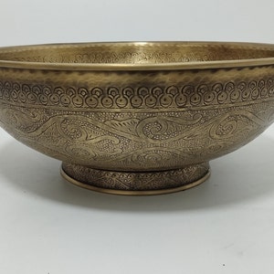Op de afbeelding: Een grote, sierlijke messing kom met een ingewikkeld gegraveerd ontwerp. De kom heeft een brede, ronde basis en een uitlopende rand.