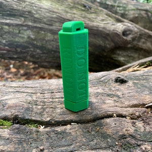 Op de afbeelding: Een groene plastic sleutelhanger met de tekst "NIET VERWIJDEREN" erop gedrukt.