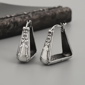 May include: A pair of silver earrings with an intricate geometric design. The earrings are shaped like a triangle with a rounded top and a pointed bottom. The earrings are made of sterling silver and have a polished finish.