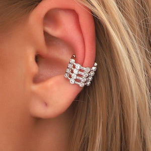 May include: A silver ear cuff with a row of clear cubic zirconia stones. The cuff is designed to wrap around the upper part of the ear.