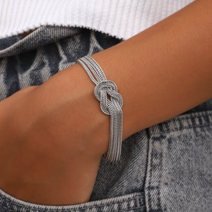 May include: A silver bracelet with a knotted design. The bracelet is made of multiple strands of chain.