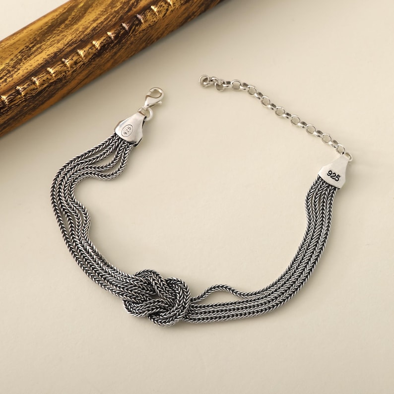 Puede incluir: Una pulsera de plata con un dise&ntilde;o de nudo y m&uacute;ltiples cadenas. La pulsera est&aacute; marcada con "925", lo que indica que est&aacute; hecha de plata de ley.