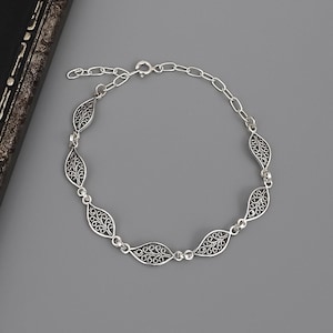 Può includere: Un bracciale color argento caratterizzato da una serie di sei maglie a forma di foglia. Ogni maglia presenta un intricato motivo a filigrana traforata. Il bracciale è collegato da piccoli anelli circolari e include una catenella di estensione.