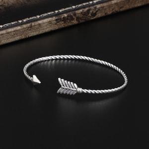 May include: Silver bracelet with a twisted rope design and an arrowhead charm.