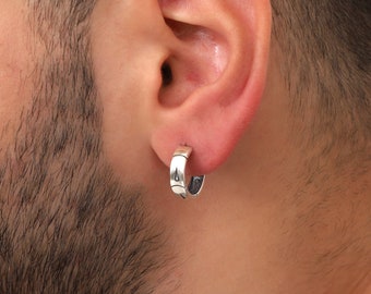 May include: A silver hoop earring with a textured design. The earring is worn in the left ear of a person.