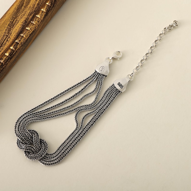 Puede incluir: Un brazalete de plata con un dise&ntilde;o anudado y m&uacute;ltiples hebras de cadena. El brazalete tiene un cierre de langosta y est&aacute; estampado con "925" en el cierre.