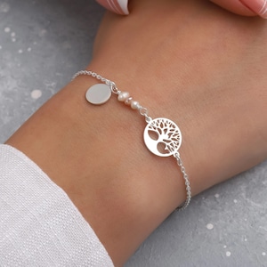 May include: A silver chain bracelet with a tree of life charm and a small round disc charm. The bracelet also features small pink beads.