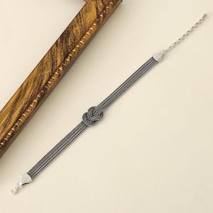 Puede incluir: Un brazalete de plata con un dise&ntilde;o anudado. El brazalete est&aacute; hecho de m&uacute;ltiples hebras de cadena.
