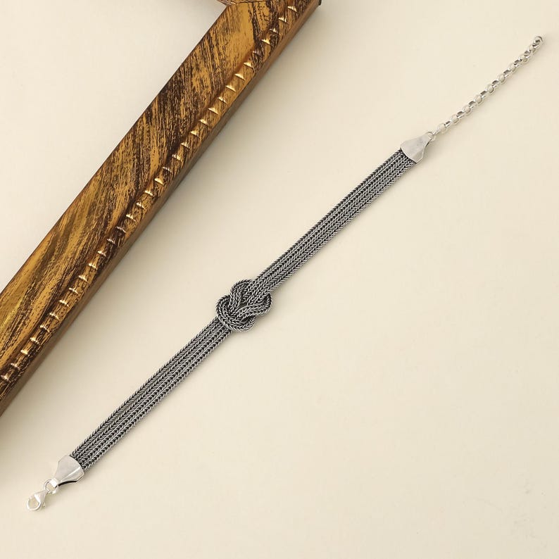 Puede incluir: Un brazalete de plata con un dise&ntilde;o anudado. El brazalete est&aacute; hecho de m&uacute;ltiples hebras de cadena.