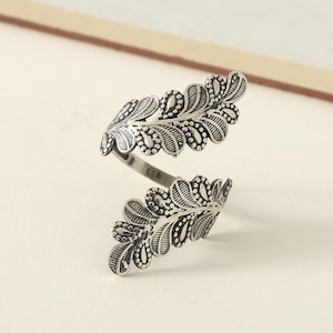 May include: A silver ring featuring a leaf design. The ring is open and adjustable.