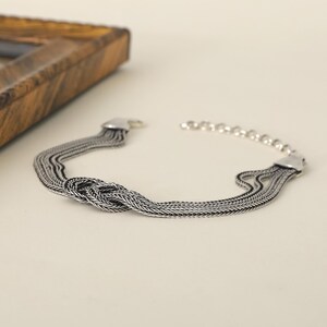 Puede incluir: Una pulsera de plata con un dise&ntilde;o anudado y m&uacute;ltiples eslabones de cadena.