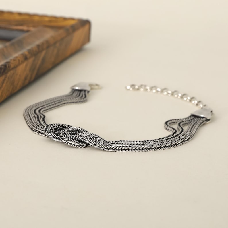 Puede incluir: Una pulsera de plata con un dise&ntilde;o anudado y m&uacute;ltiples eslabones de cadena.