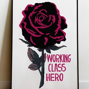 May include: A framed art print featuring a stylized black rose with magenta outlines and accents. The artwork includes the text "WORKING CLASS HERO" in magenta. The rose has green leaves and stem against a white background.