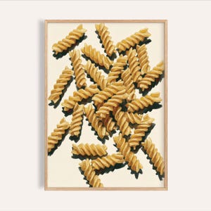 May include: A framed art print featuring a close-up of fusilli pasta. The pasta is a golden-yellow color, with each piece casting a dark shadow. The background is a light cream color, and the frame is a light wood color.