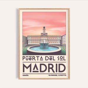 May include: A framed art print featuring a stylized illustration of Puerta del Sol in Madrid, Spain. The artwork showcases a building with a clock tower, a fountain, and the text "Puerta del Sol Madrid España". The sky is a gradient of pink and orange.