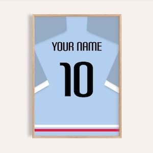 May include: Framed print of a light blue jersey with the number 10 in black. The words "YOUR NAME" are above the number. The jersey design includes white and red stripes at the bottom and is set in a wooden frame.