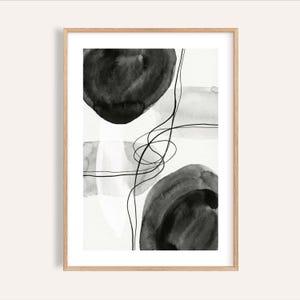 May include: Abstract art print in a wooden frame. The artwork features black and gray watercolor shapes and lines on a white background. The design includes two large, dark circular shapes and a series of intersecting lines.