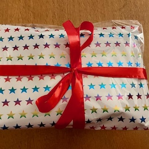 May include: A white gift box with a rainbow star pattern wrapped with a red ribbon. The box is tied with a bow.