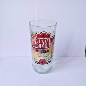 Könnte beinhalten: Ein klares Bierglas mit dem Logo "Desperados Original" in Rot und Weiß. Das Glas hat ein farbenfrohes Design und den Text "Beer-Biere" und "Aguardiente". Das Glas ist 650 ml.