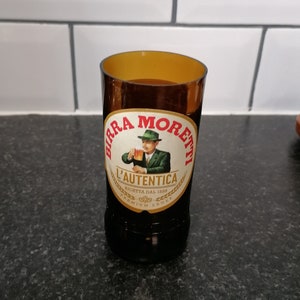 Puede incluir: Vaso para beber hecho de una botella de cerveza Birra Moretti reciclada. El vaso marrón conserva la etiqueta original con el logotipo de Birra Moretti y un hombre con traje y sombrero verdes. Artículo reciclado único.