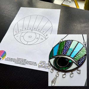 Puede incluir: Un colgante de ojo de vidriera con piezas de vidrio azul, verde y blanco, acentuado con colgantes de cristal transparente. Un patrón de papel con secciones numeradas está al lado. El texto dice "Personal Use Only!"