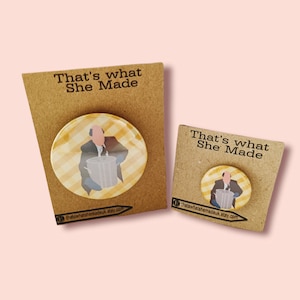 May include: Two round buttons with a yellow and white chequered background. The buttons feature a cartoon image of a man holding a bin. The text "That's what She Made" is printed on the brown card stock behind the buttons.