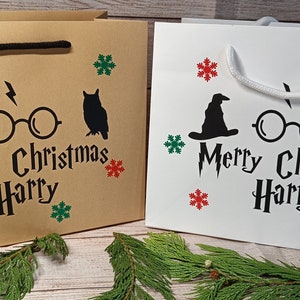 May include: Two gift bags, one tan and one white, with black graphics and the text "Merry Christmas Harry." The bags feature a wizard hat, glasses, and an owl, with red and green snowflake accents. Black handles.