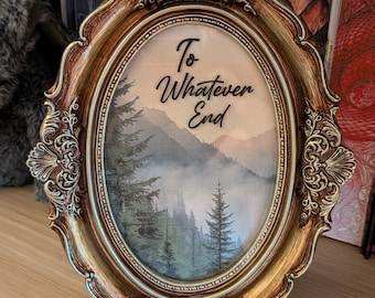 May include: An oval-shaped picture frame with an ornate, metallic gold and bronze finish. Inside, a print depicts a misty mountain landscape with evergreen trees. The text "To Whatever End" is printed in black script across the upper portion.