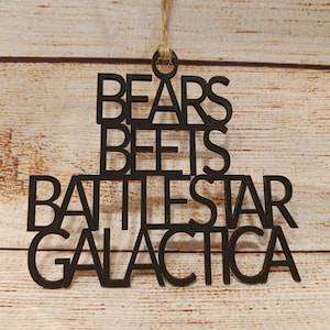 May include: Black wooden ornament with the words "Bears Beets Battlestar Galactica" written on it.
