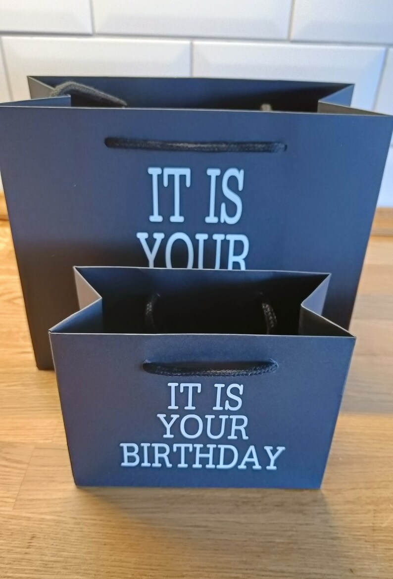 May include: Two black gift bags with white text. The larger bag says "It is your" and the smaller bag says "It is your birthday".