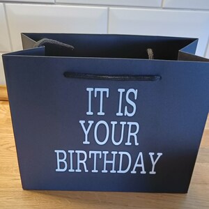 May include: Black gift bag with white text that reads "It is your birthday".