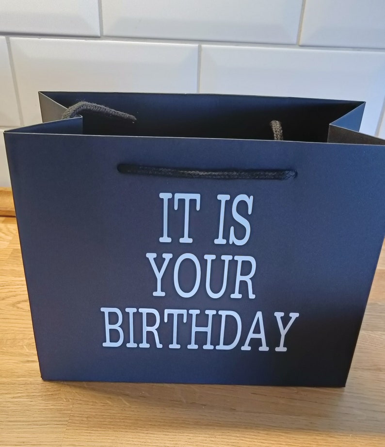 May include: Black gift bag with white text that reads "It is your birthday".
