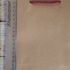 May include: A brown paper gift bag with red rope handles. The bag has the words "Shatterproof" printed on the side.