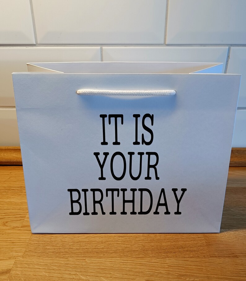 May include: White gift bag with black text that reads "It is your birthday".