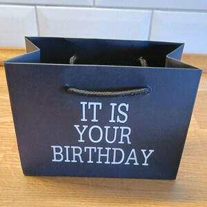 May include: Black gift bag with white text that reads "It is your birthday".