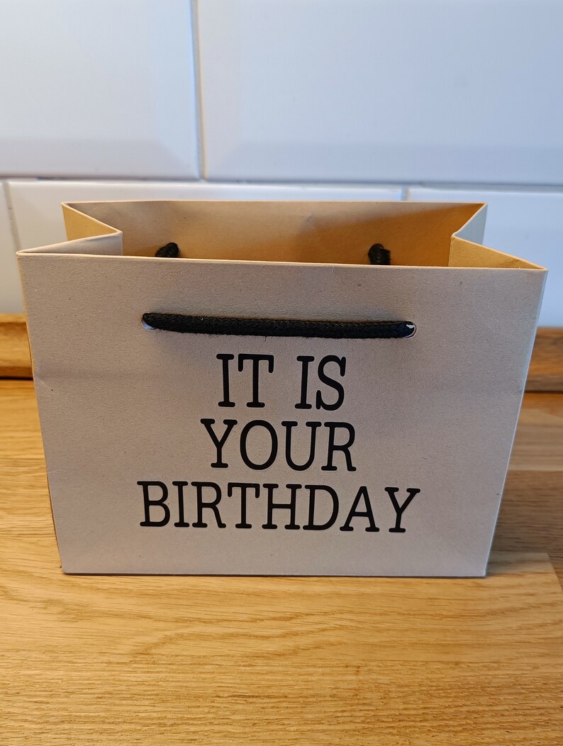 May include: A brown paper gift bag with black handles and the text "IT IS YOUR BIRTHDAY" printed on the front.