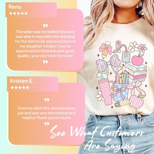 May include: A cream-colored t-shirt featuring a colorful graphic print of school supplies including a pencil, a stack of books, a pink apple, a tumbler, and bows. The design is accented with small stars and flowers in shades of pink, blue, and yellow.