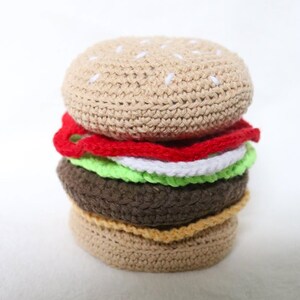 May include: A crocheted hamburger toy with a brown bun, red ketchup, white cheese, green lettuce, and a tan bottom bun.