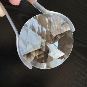 May include: A clear crystal prism with a faceted design. The prism is being held by a pair of clear plastic tweezers.
