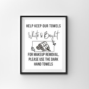 May include: Black and white sign with the text "HELP KEEP OUR TOWELS White & Bright" and a graphic of rolled up towels. The sign also says "FOR MAKEUP REMOVAL, PLEASE USE THE DARK HAND TOWELS".