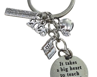May include: Silver-coloured keychain with various charms: a ruler, an apple, a book, and a circular charm inscribed with "It takes a big heart to teach little minds." A teacher appreciation gift.